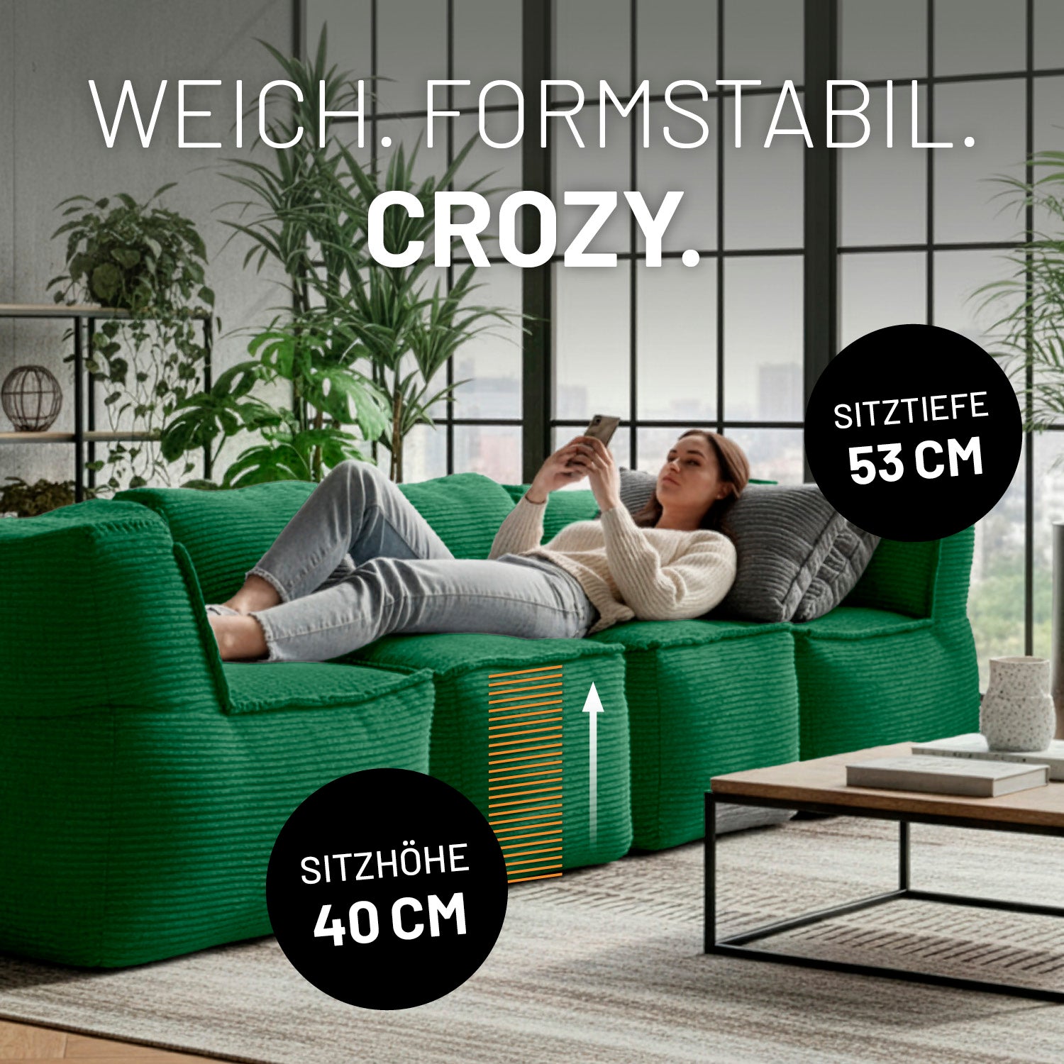 Modulare dunkelgrüne Lounge-Sitzlandschaft mit 40 cm Sitzhöhe und 53 cm Sitztiefe, auf der eine Frau entspannt liegend ihr Smartphone nutzt.