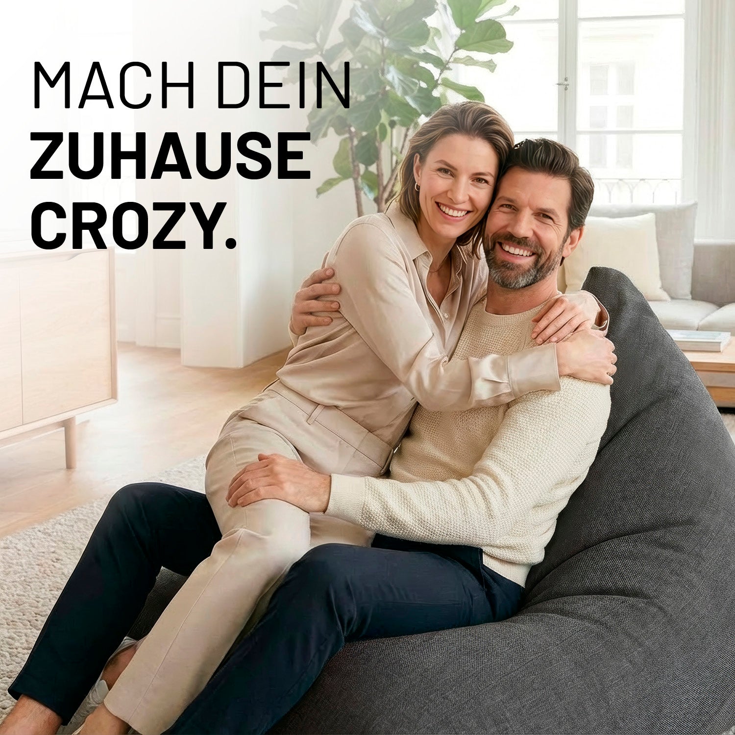 Ein lachendes Paar umarmt sich auf dem Interior Line Sitzsack in Dunkelgrau im hellen Wohnzimmer; Schriftzug „Mach dein Zuhause crozy.“