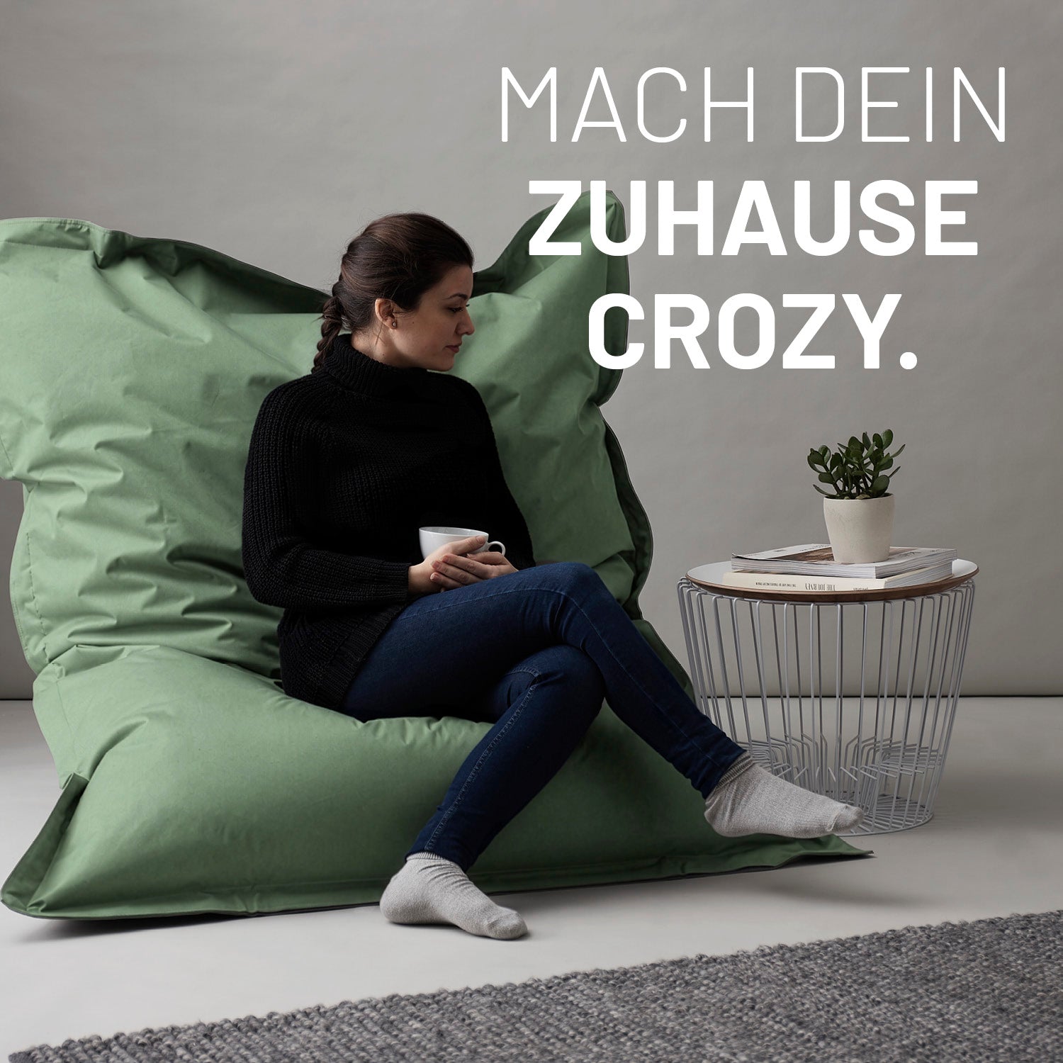 Eine Frau sitzt auf dem pastellgrünen XXL Sitzsack, eine Tasse in der Hand, neben ihr ein Tisch - Mach dein Zuhause crozy.