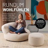 Eine Frau sitzt in einem modernen Wohnzimmer auf dem Sitzsack Lounge-Sofa aus der LUMALAND Teddy-Reihe, Hocker und Beistelltisch daneben.