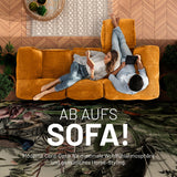 Frau mit Buch und Mann mit Tablet enspannen auf dem senfgelben Cord-Sitzsack-Sofa in einem modernen Wohnzimmer aus der Vogelperspektive. 