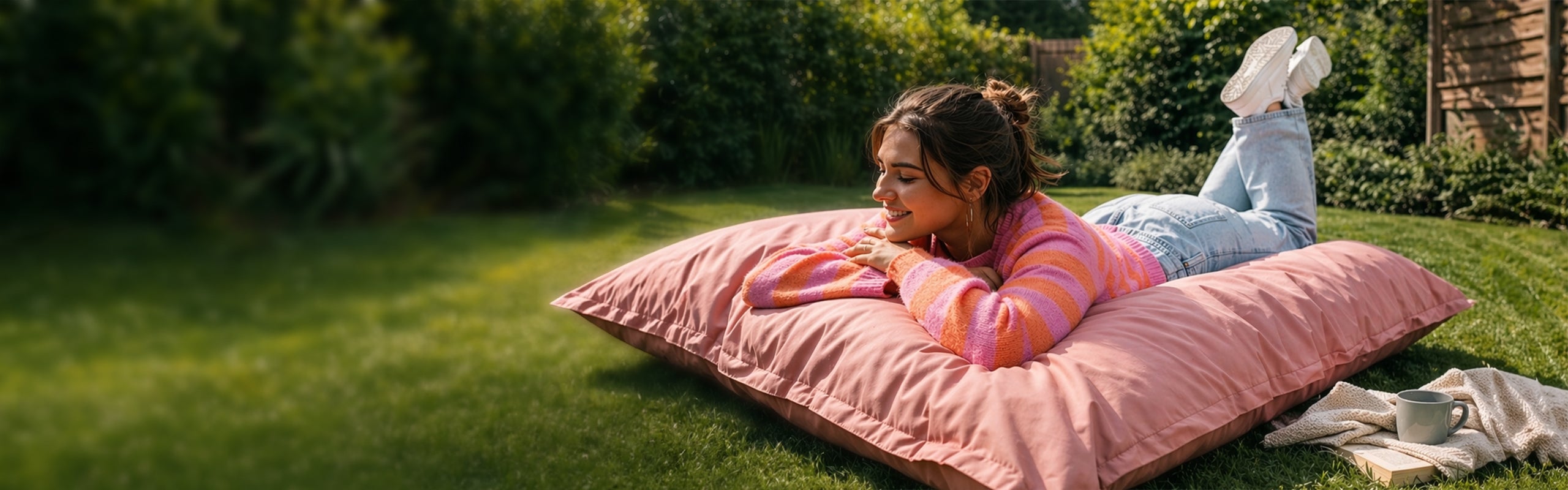 Frau liegt entspannt auf einem großen XXL Sitzsack in Pastellpink im Garten, genießt die Sonne und nutzt ihn bequem als Outdoor-Liegefläche zum Relaxen.