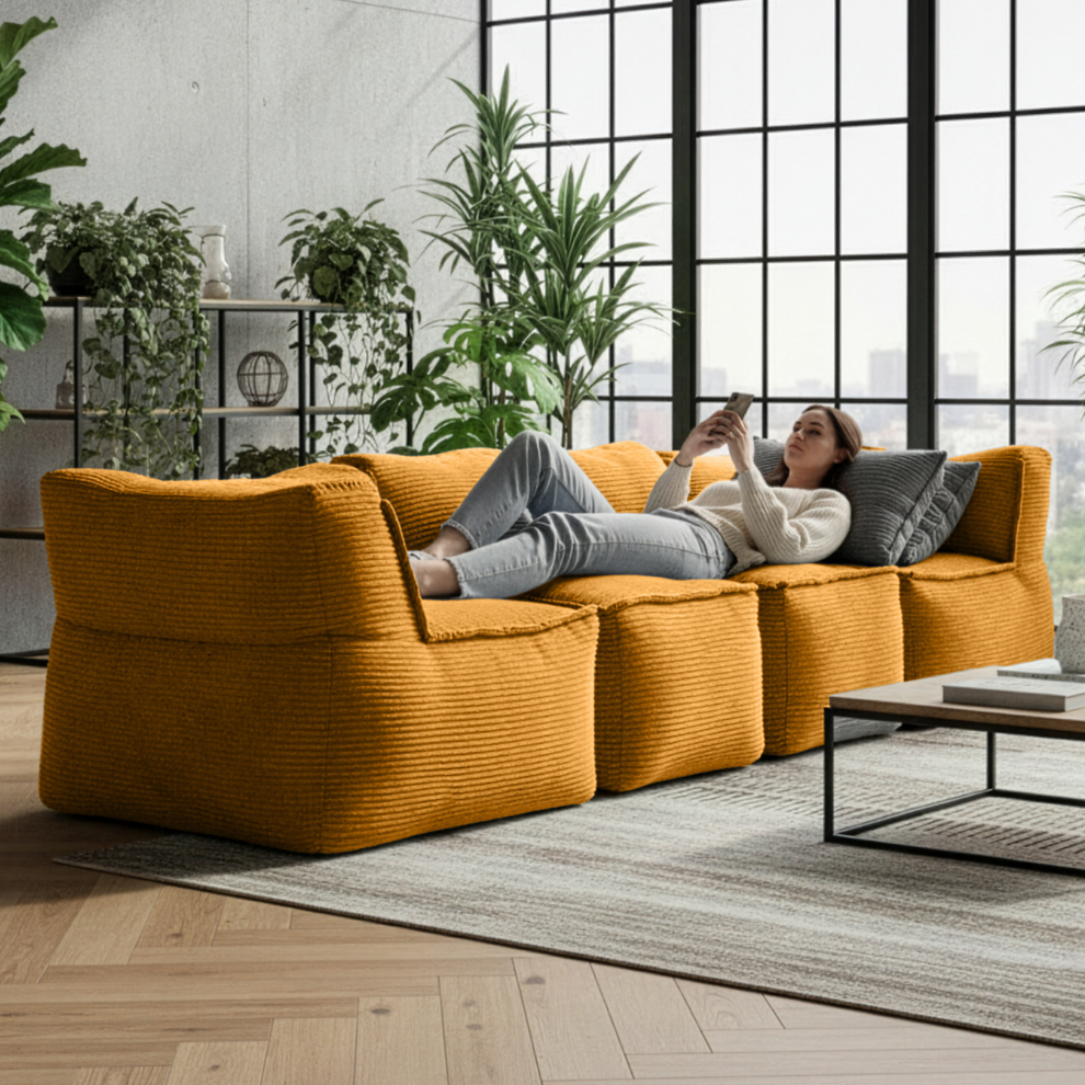 Modulares LUMALAND Sitzsystem in Senfgelb: mehrere Cord-Module als Sofa kombiniert, eine Frau entspannt liegend im modernen Wohnraum mit Pflanzen.