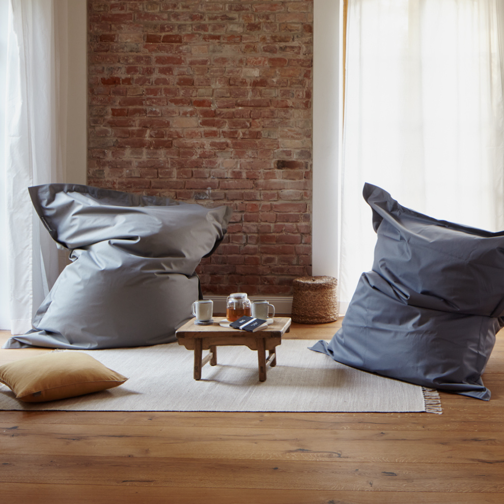 Zwei graue XXL-Sitzsäcke in gemütlichem Wohnraum mit Backsteinwand, kleinem Holztisch, Kissen und Teetassen auf hellem Teppich.