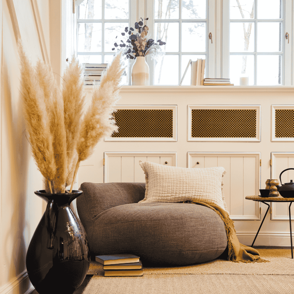 Graues LUMALAND Sitzsack-Sofa der Interior Line steht gemütlich im Wohnzimmer vor Fensterbank mit Deko, Kissen und Decke, ergänzt durch Vase und Beistelltisch.