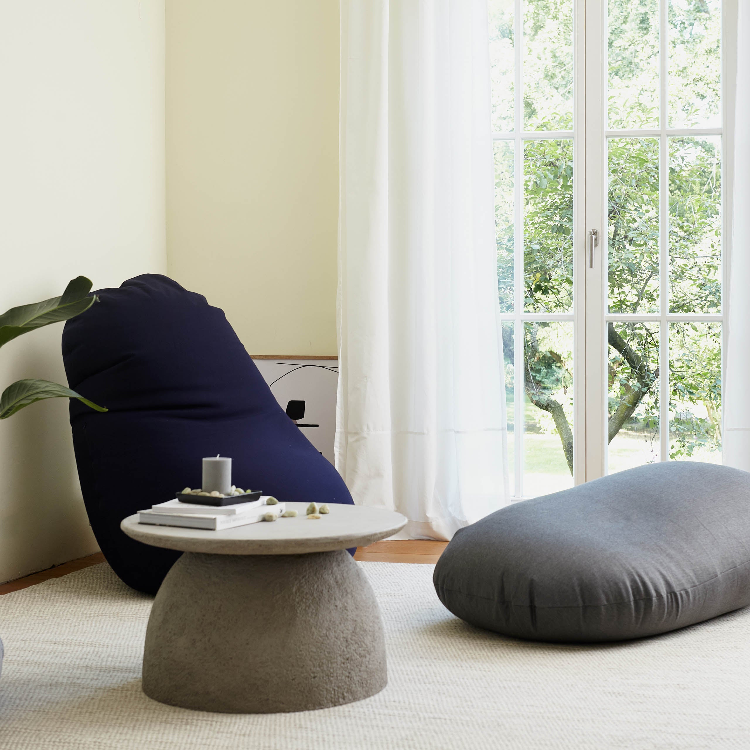 Flexi Comfort Sitzsack in Navyblau als Sitzkissen und in Dunkelgrau als Liegekissen in einem lichtdurchfluteten Wohnzimmer.
