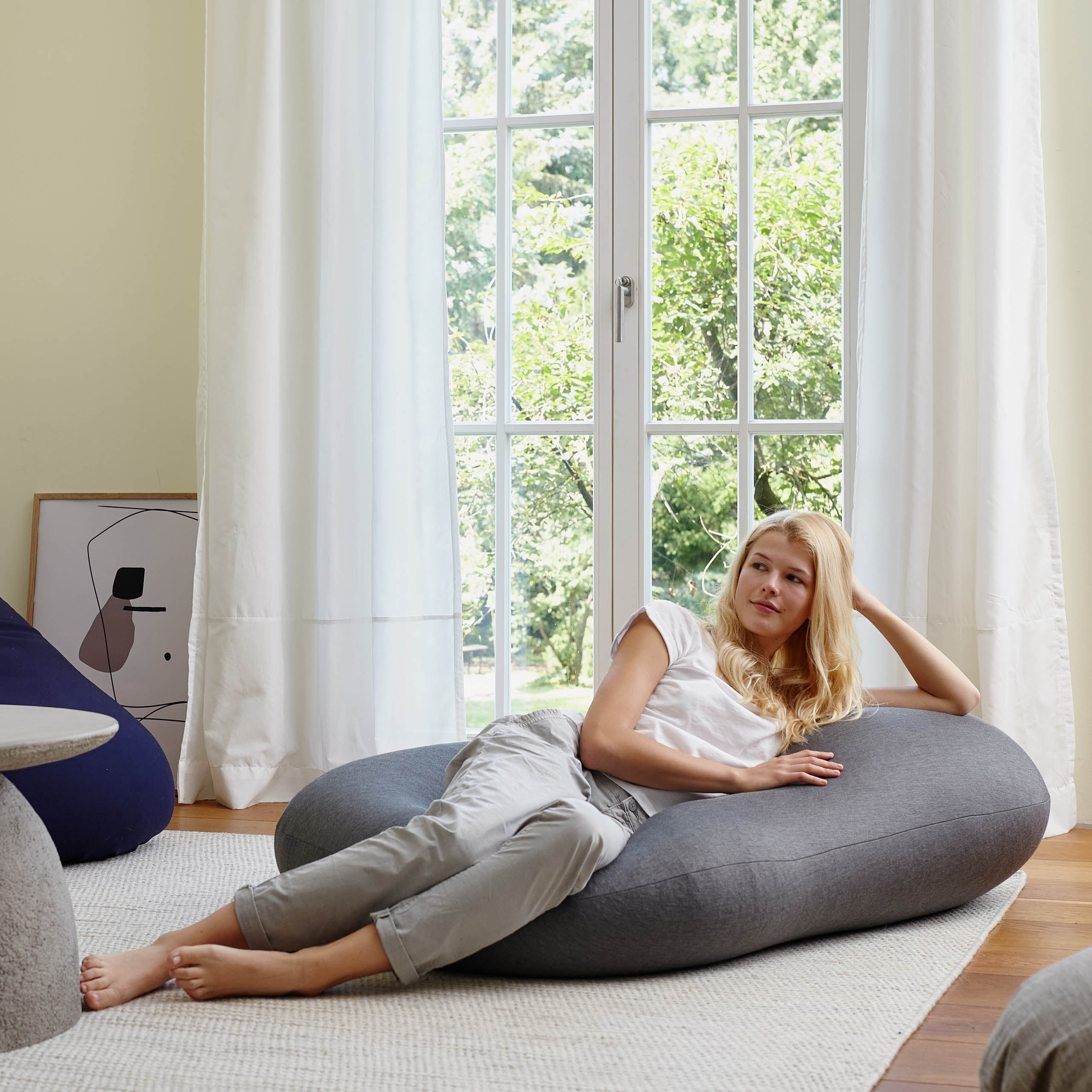 Ein Frau liegt mit in ihrer Hand abgestützen Kopf auf dem dunkelgrauen Flexi Comfort Sitzsack als Liegekissen.