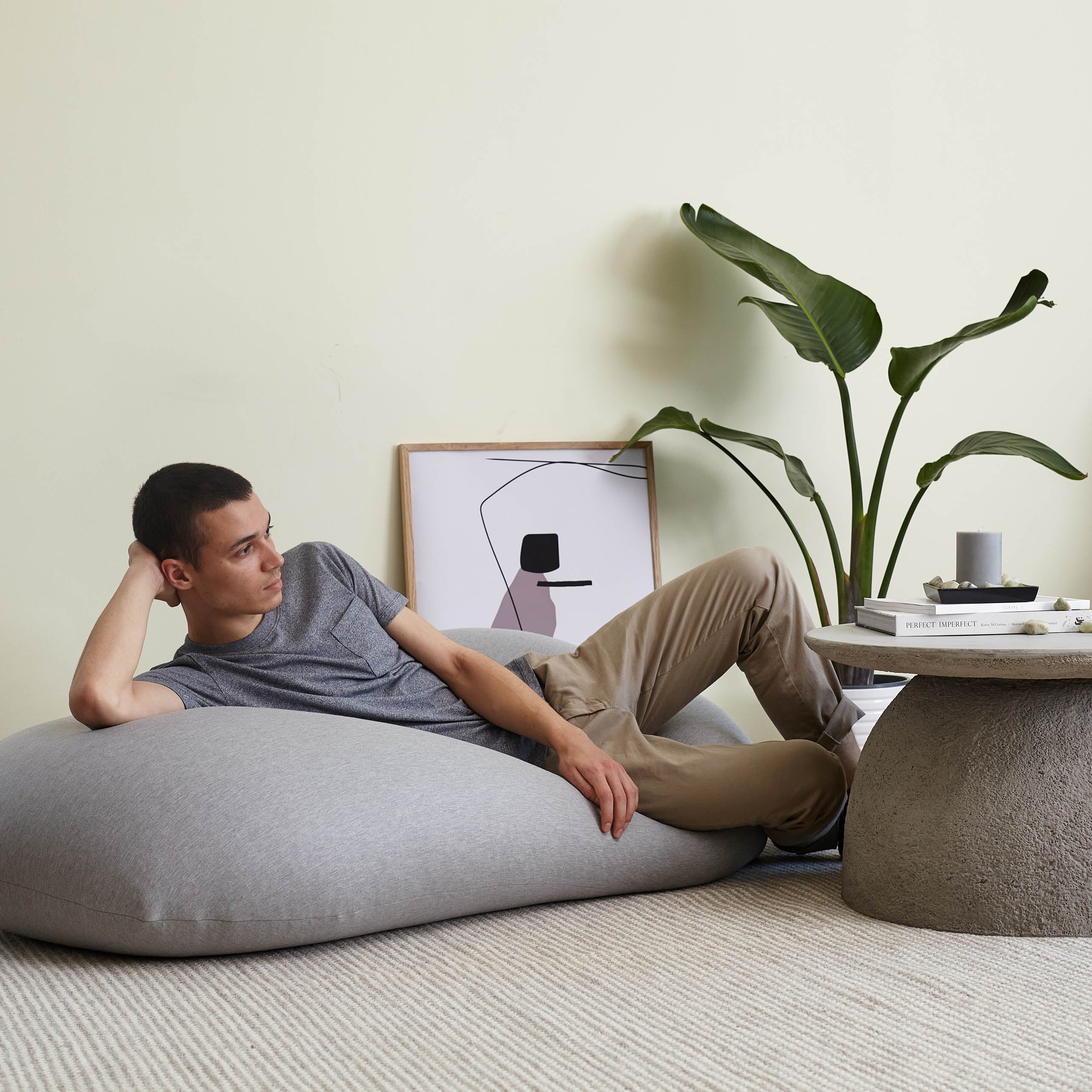 Ein Mann liegt mit in seiner Hand abgestützen Kopf auf dem hellgrauen Flexi Comfort Liege-Sitzsack.